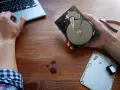 Ręce majstrują przy dysku HDD, obok laptop i kombinerki. Dowiedz się, jak przyspieszyć dysk HDD.