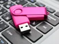 Różowy pendrive leży na klawiaturze, gotowy do pracy jak przenośny dysk twardy.