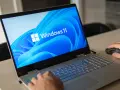 Pierwsze uruchomienie komputera z systemem Windows 11. Dłoń użytkownika przesuwa myszkę, a ekran laptopa wyświetla logo systemu.