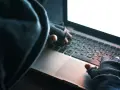 Osoba w kapturze i rękawiczkach pisze na laptopie. To może być przykład kradzieży tożsamości.