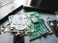 Jak dołożyć RAM do laptopa Dell? Na zdjęciu widać płytę główną, moduły RAM, dysk twardy i fragment laptopa.