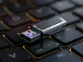 Srebrny pendrive na klawiaturze. Dowiedz się, jak zaszyfrować pendrive, by chronić swoje dane.