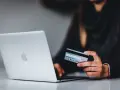 Kobieta z kartą kredytową przy laptopie. Dowiedz się, jak bezpiecznie korzystać z komputera podczas zakupów online.