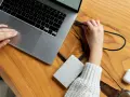 Podłączanie drugiego dysku SSD do komputera jest proste. Na zdjęciu widać, jak ręka podłącza kabel do laptopa, przygotowując się do rozszerzenia pamięci.