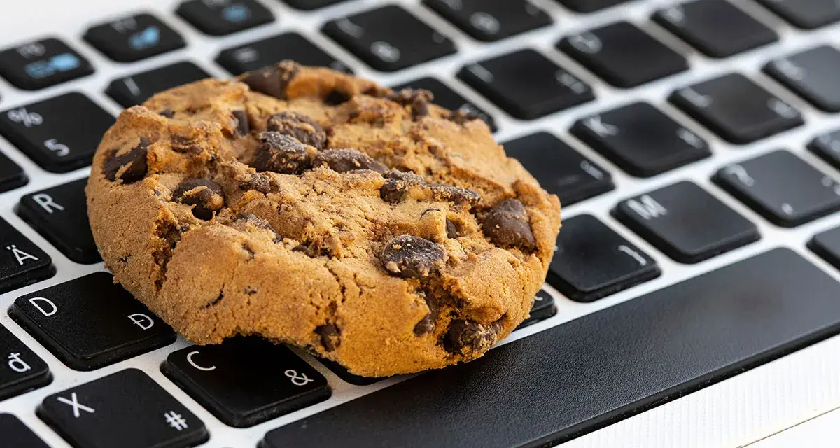 Ciasteczko z kawałkami czekolady leży na klawiaturze laptopa. Czy to są ciasteczka, które śledzą Twoje kliknięcia?