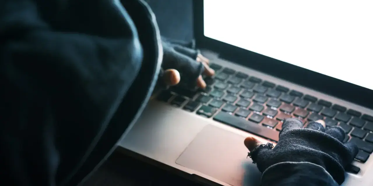 Osoba w kapturze i rękawiczkach pisze na laptopie. To może być przykład kradzieży tożsamości.