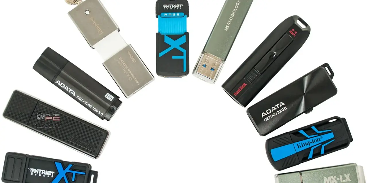 Różne modele pendrive'ów, czyli przenośnych pamięci USB, ułożone w łuk. Widać marki Kingston, ADATA, SanDisk, Patriot, Transcend, MX-TECHNOLOGY.