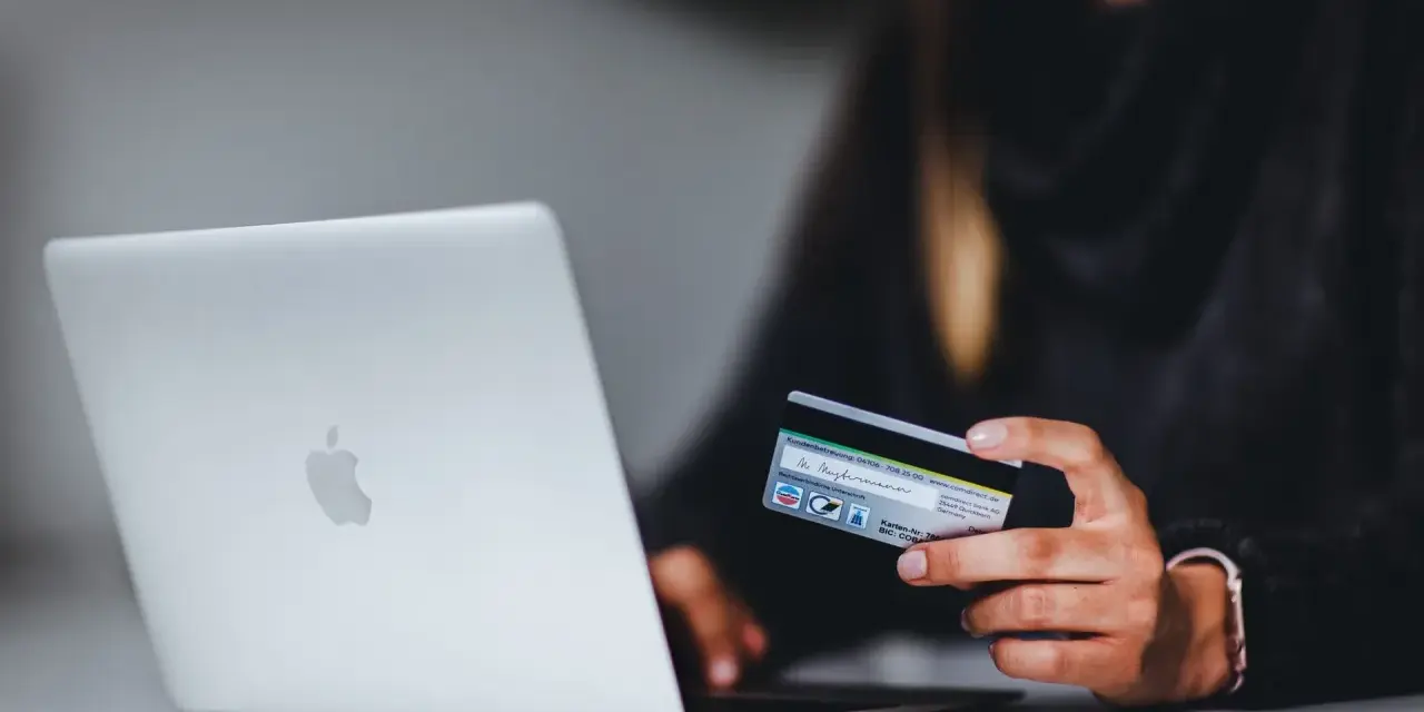 Kobieta z kartą kredytową przy laptopie. Dowiedz się, jak bezpiecznie korzystać z komputera podczas zakupów online.