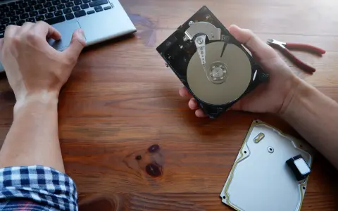Ręce majstrują przy dysku HDD, obok laptop i kombinerki. Dowiedz się, jak przyspieszyć dysk HDD.