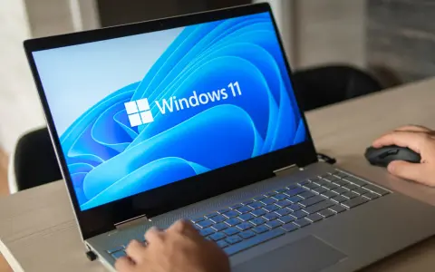 Pierwsze uruchomienie komputera z systemem Windows 11. Dłoń użytkownika przesuwa myszkę, a ekran laptopa wyświetla logo systemu.