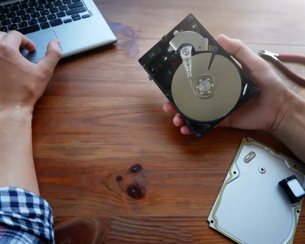 Ręce majstrują przy dysku HDD, obok laptop i kombinerki. Dowiedz się, jak przyspieszyć dysk HDD.