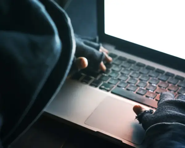 Osoba w kapturze i rękawiczkach pisze na laptopie. To może być przykład kradzieży tożsamości.