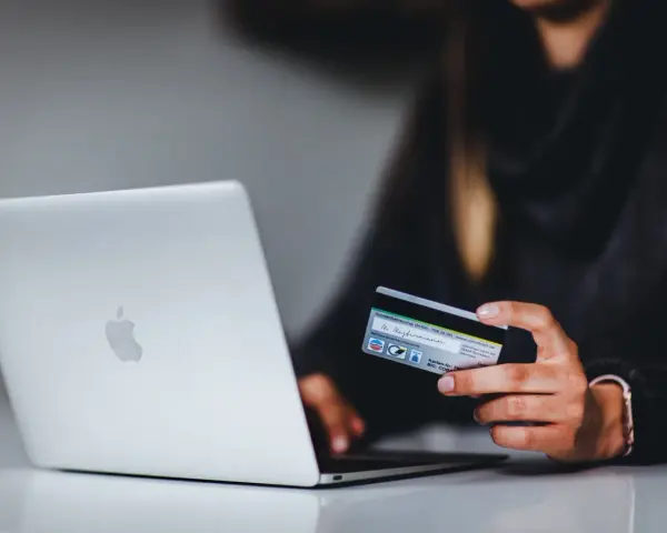 Kobieta z kartą kredytową przy laptopie. Dowiedz się, jak bezpiecznie korzystać z komputera podczas zakupów online.