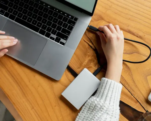 Podłączanie drugiego dysku SSD do komputera jest proste. Na zdjęciu widać, jak ręka podłącza kabel do laptopa, przygotowując się do rozszerzenia pamięci.