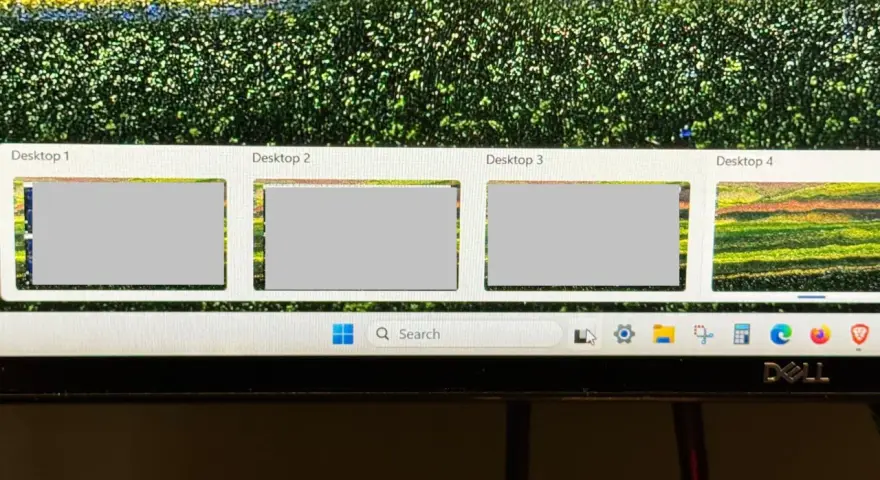 Widok czterech pulpitów Windows 10, z czego trzy są szare, a czwarty pokazuje kolorowy krajobraz. Pasek zadań z wyszukiwarką i ikonami.