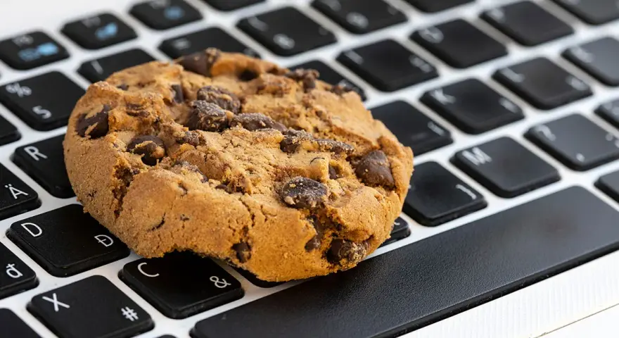 Ciasteczko z kawałkami czekolady leży na klawiaturze laptopa. Czy to są ciasteczka, które śledzą Twoje kliknięcia?