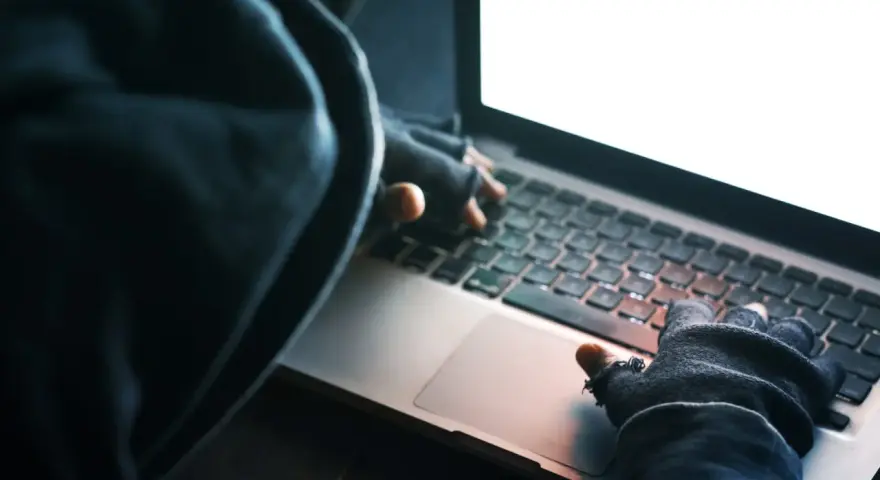 Osoba w kapturze i rękawiczkach pisze na laptopie. To może być przykład kradzieży tożsamości.