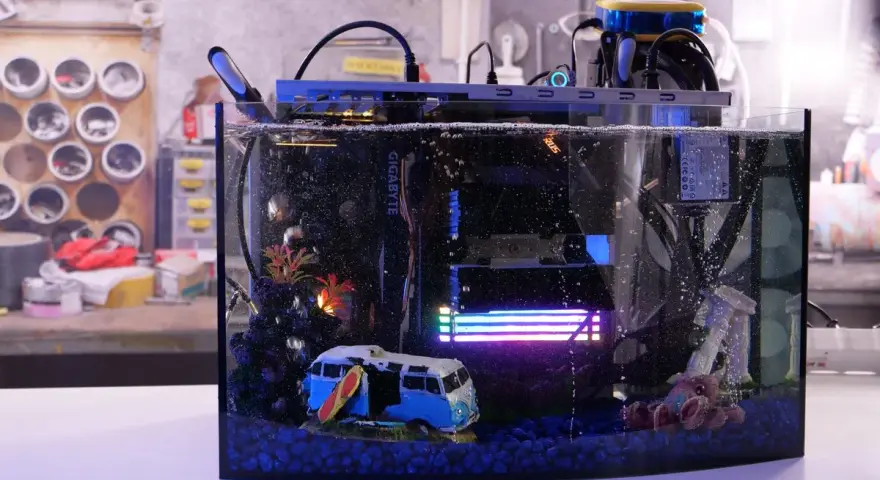 Komputer w akwarium z chłodzeniem cieczą, zanurzony w oleju mineralnym. W środku miniaturowy kamper i surfer.