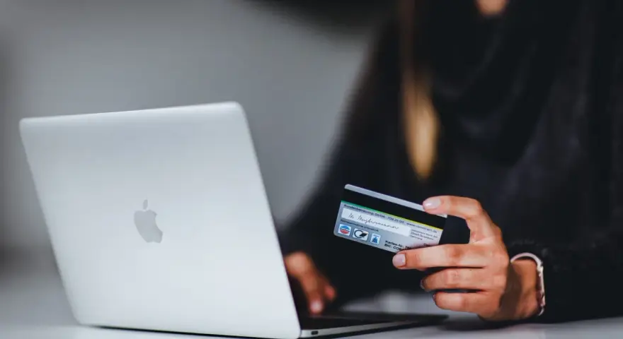 Kobieta z kartą kredytową przy laptopie. Dowiedz się, jak bezpiecznie korzystać z komputera podczas zakupów online.