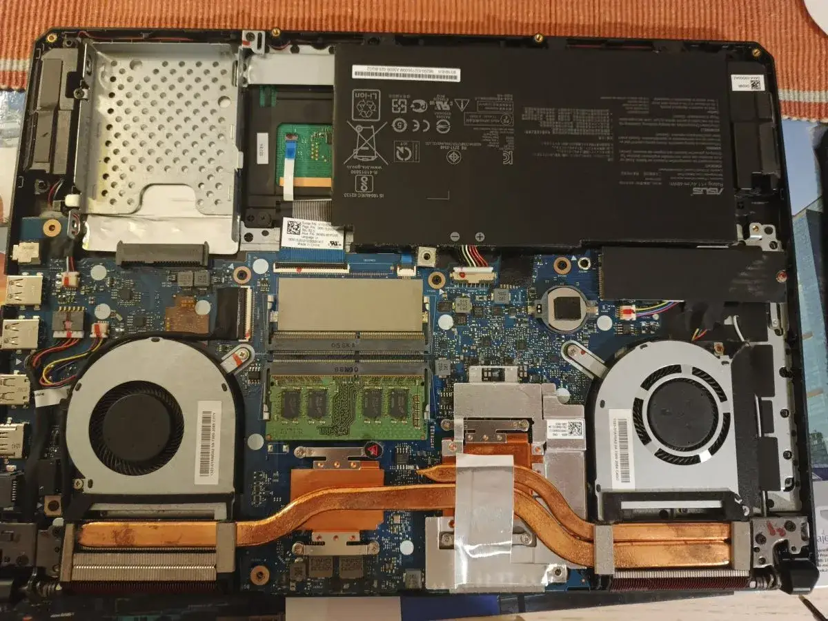 Wnętrze laptopa z widocznym ram w laptopie, baterią, wentylatorami i płytą główną.
