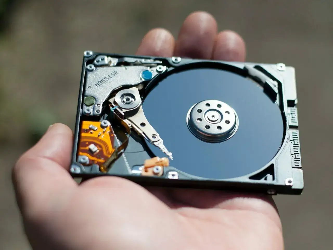 Otwarty dysk HDD w dłoni. Zastanawiasz się, jak przyspieszyć dysk HDD? Oto jego wnętrze.