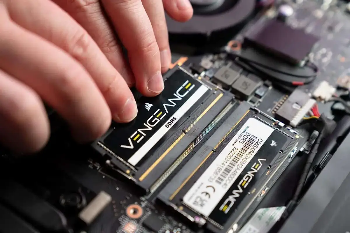 Dłonie montują moduł pamięci RAM DDR5 Vengeance w laptopie. Wymiana pamięci RAM w laptopie to prosty sposób na zwiększenie jego wydajności.